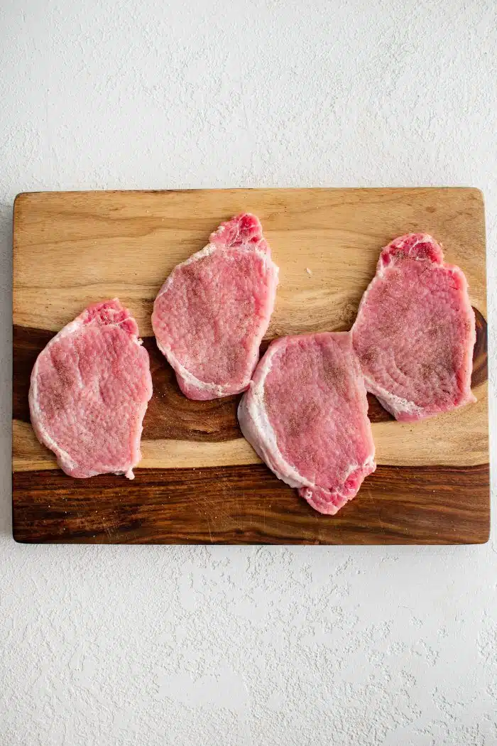 Four pounded thin pork loin chops on a cutting board.