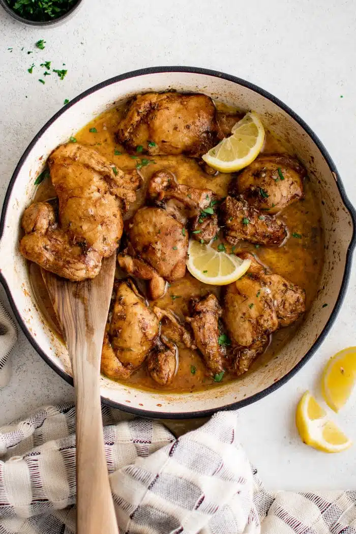 Large skillet filled with baked balsamic chicken thighs garnished with sliced lemon.