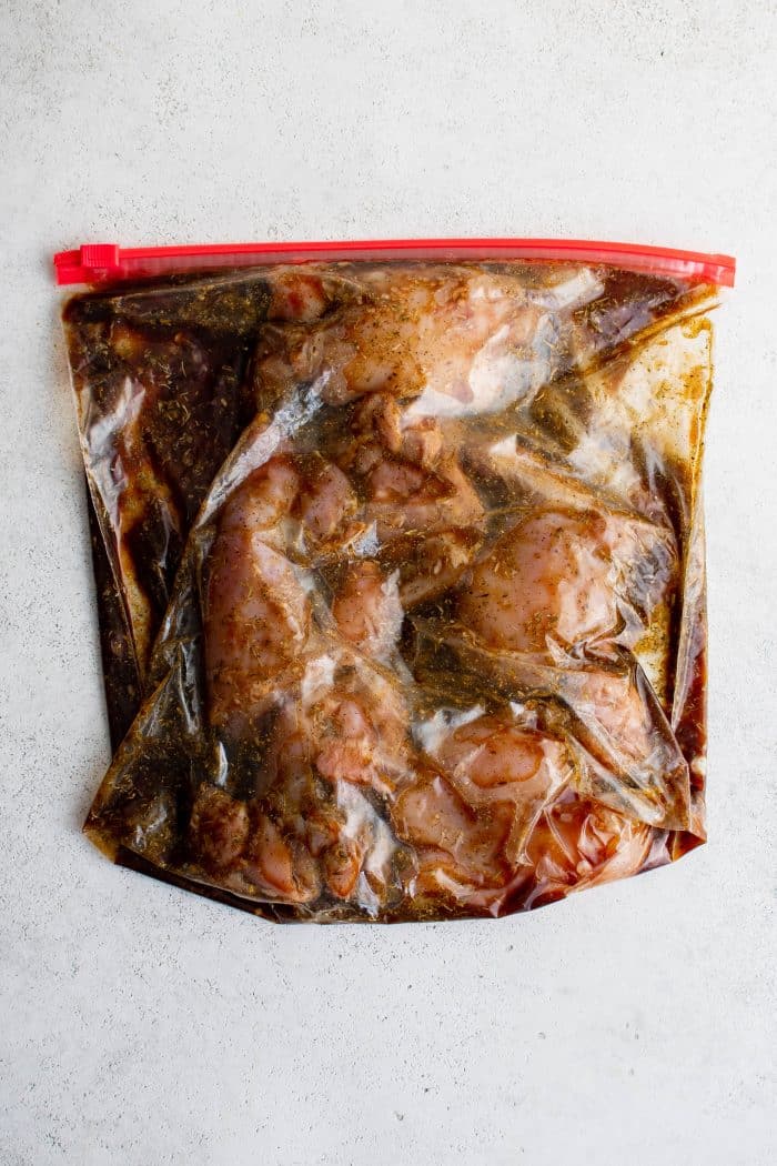 Large heavy duty ziplock bag with chicken thighs and balsamic vinegar marinade sealed and lying flat on a white surface.