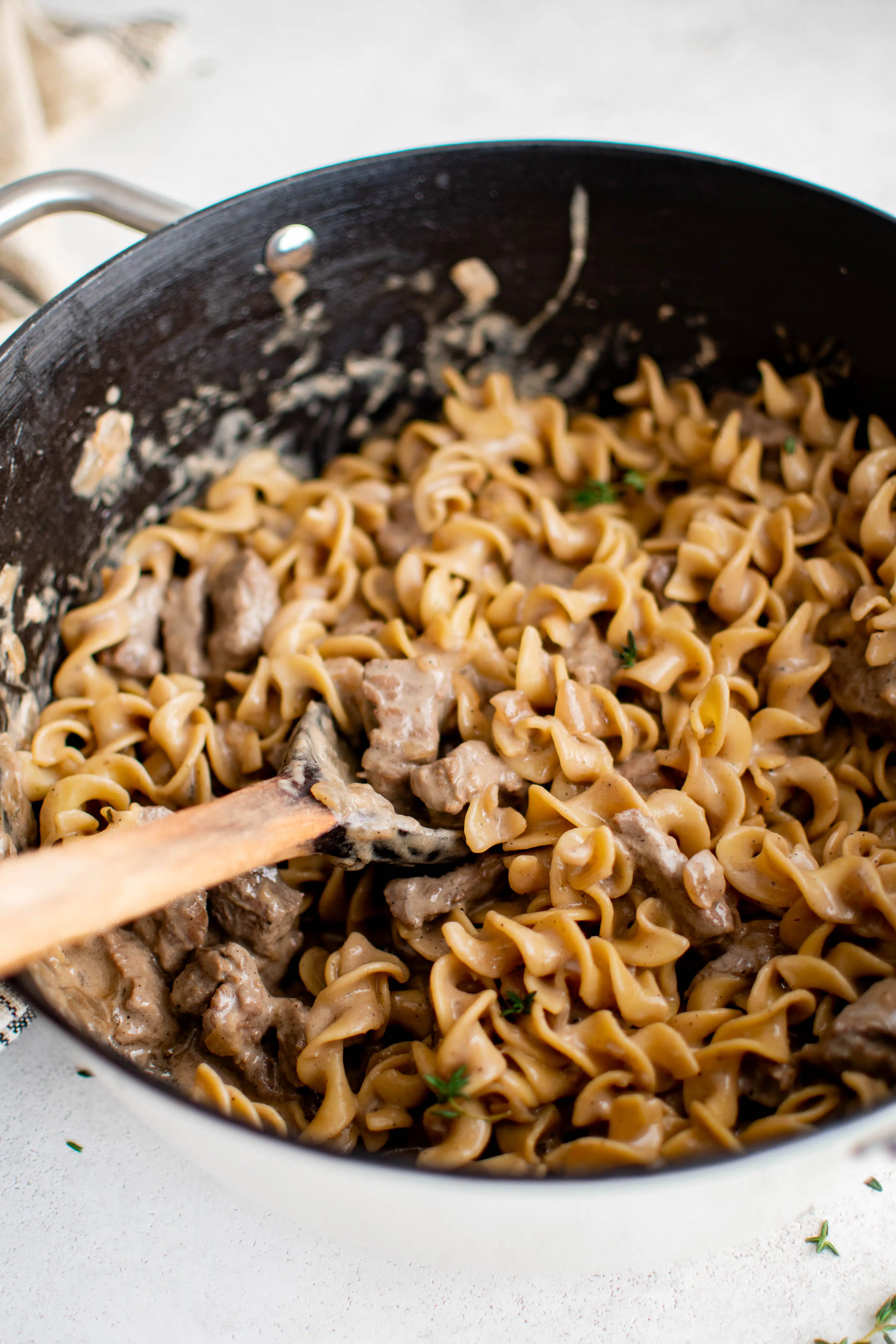 Large ceramic pot filled with cooked beef chunks and egg noodles tossed in a homemade creamy brown gravy.
