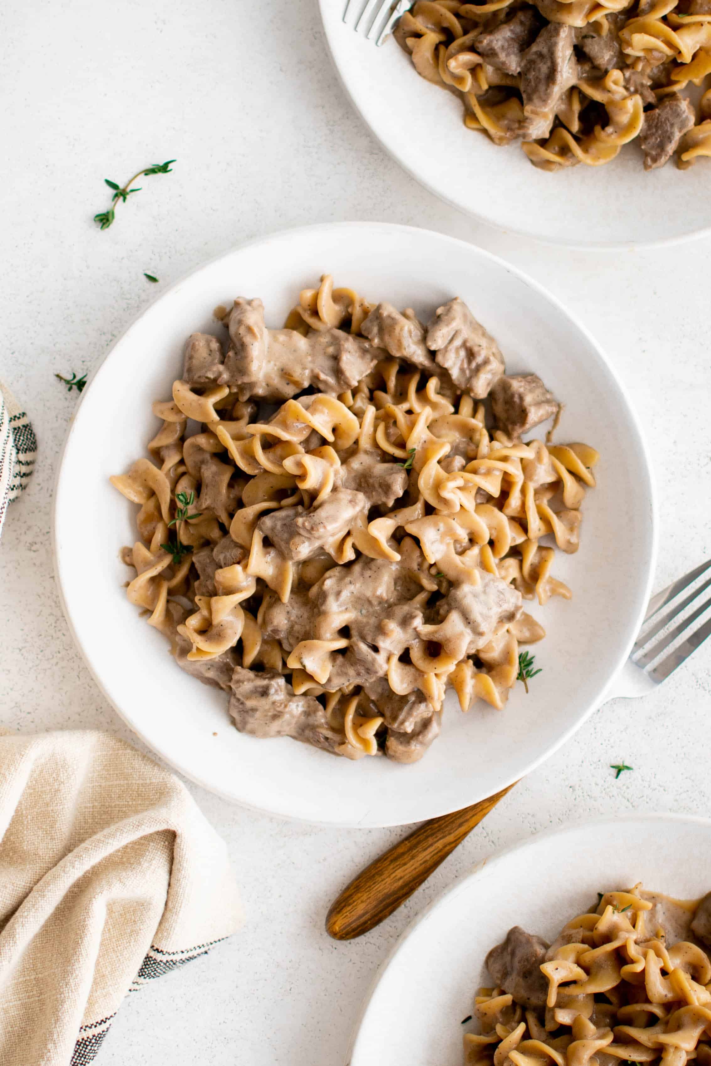 Overhead image of a white plate filled with chunks of meat and egg noodles smothered in a creamy brown gravy and garnished with fresh thyme.