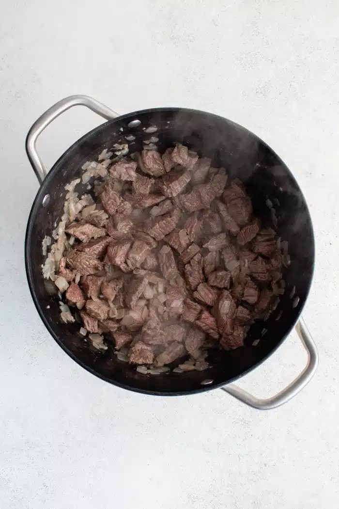 Pieces of beef chuck, diced onion, and garlic cooking in a large pot.