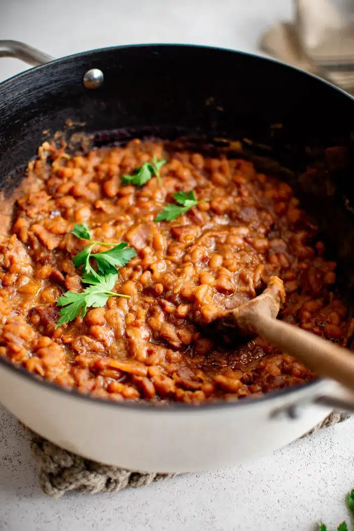 Thicked Boston baked beans with bacon in a large pot garnished with fresh parsley.