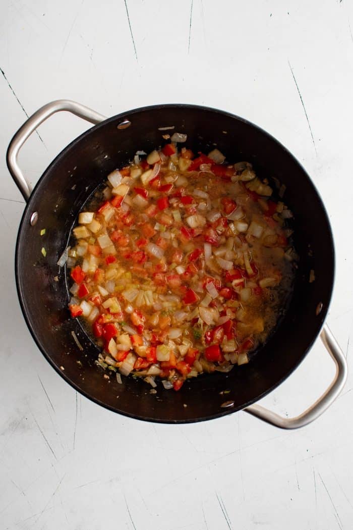 White wine added to mixture of crushed tomatoes, garlic, onions, fennel, and leek softened and cooking in a large pot.
