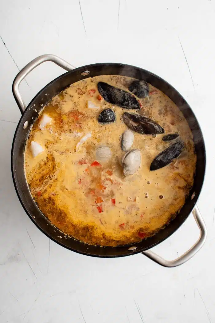 Large pot of simmering soup filled with fish, mussels, clams.