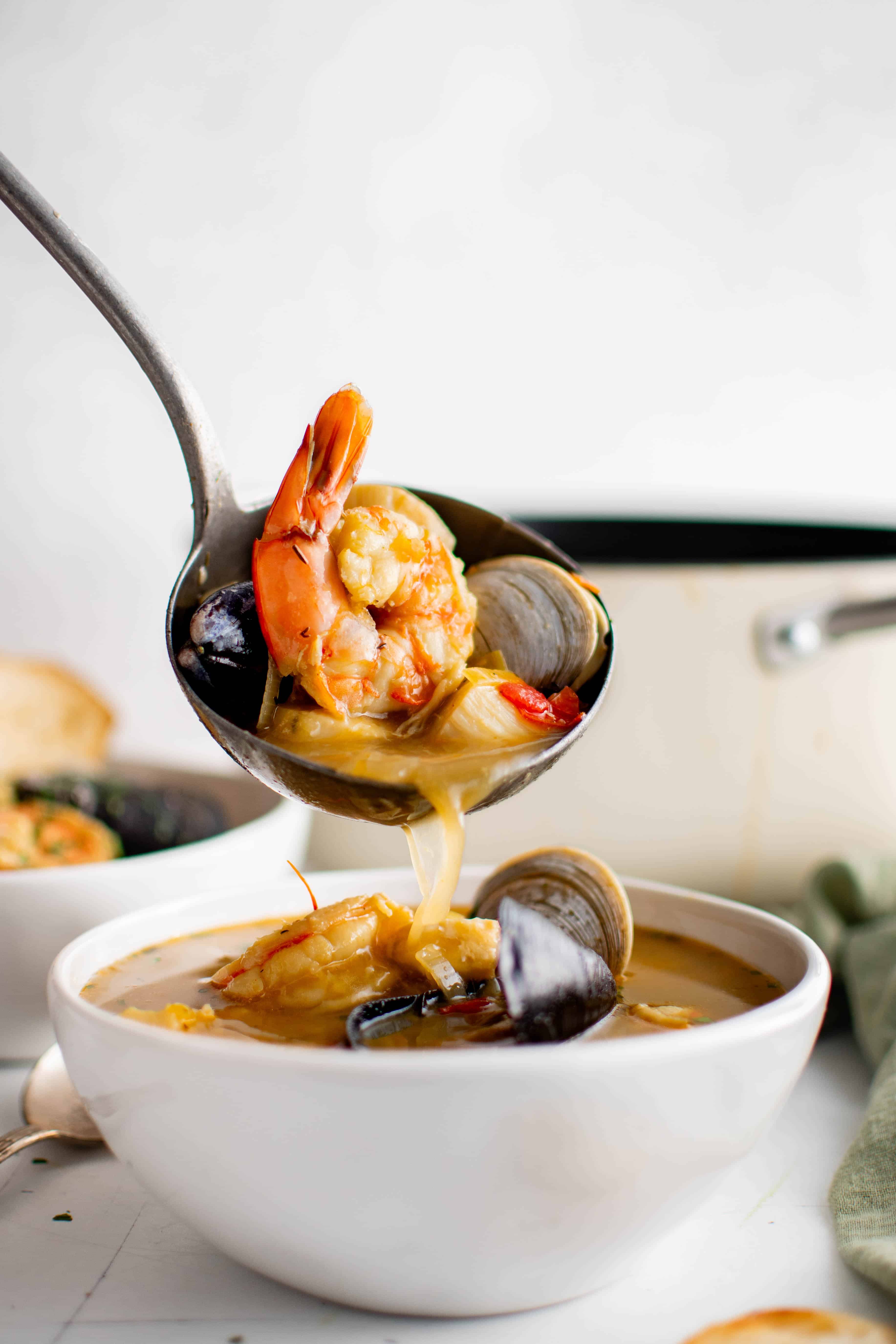 Large ladle filled with homemade Bouillabaisse  made with shrimp, mussels, and clams being poured into a white soup bowl.