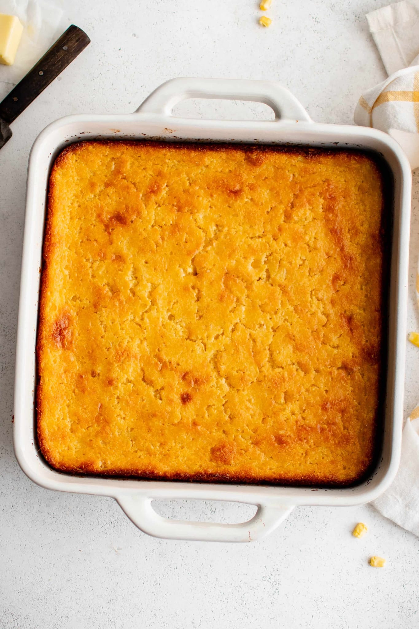 Overhead image of a white 9-by-9 inch baking dish filled with baked Jiffy cornbread casserole with a golden brown crust.