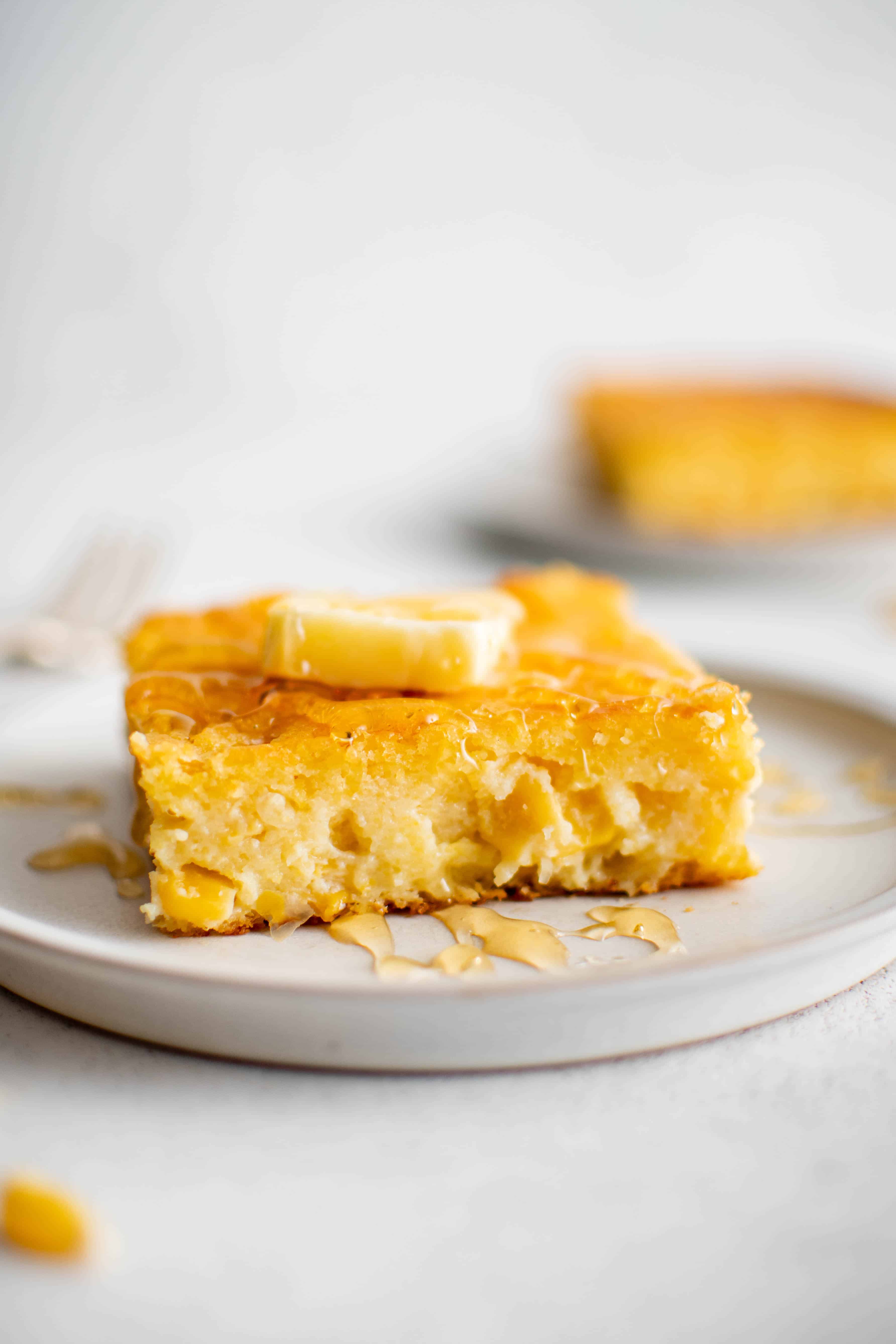 Image of a plate with a square slice of cornbread casserole topped with butter.