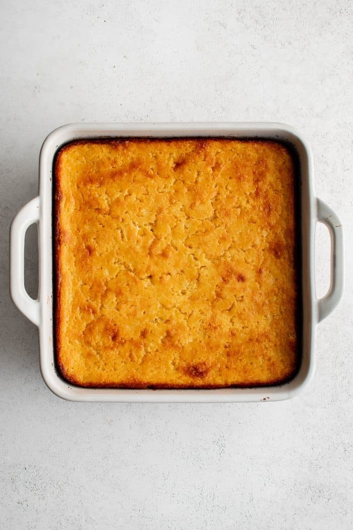 A white 9-by-9 inch baking dish filled with a baked Jiffy cornbread casserole.