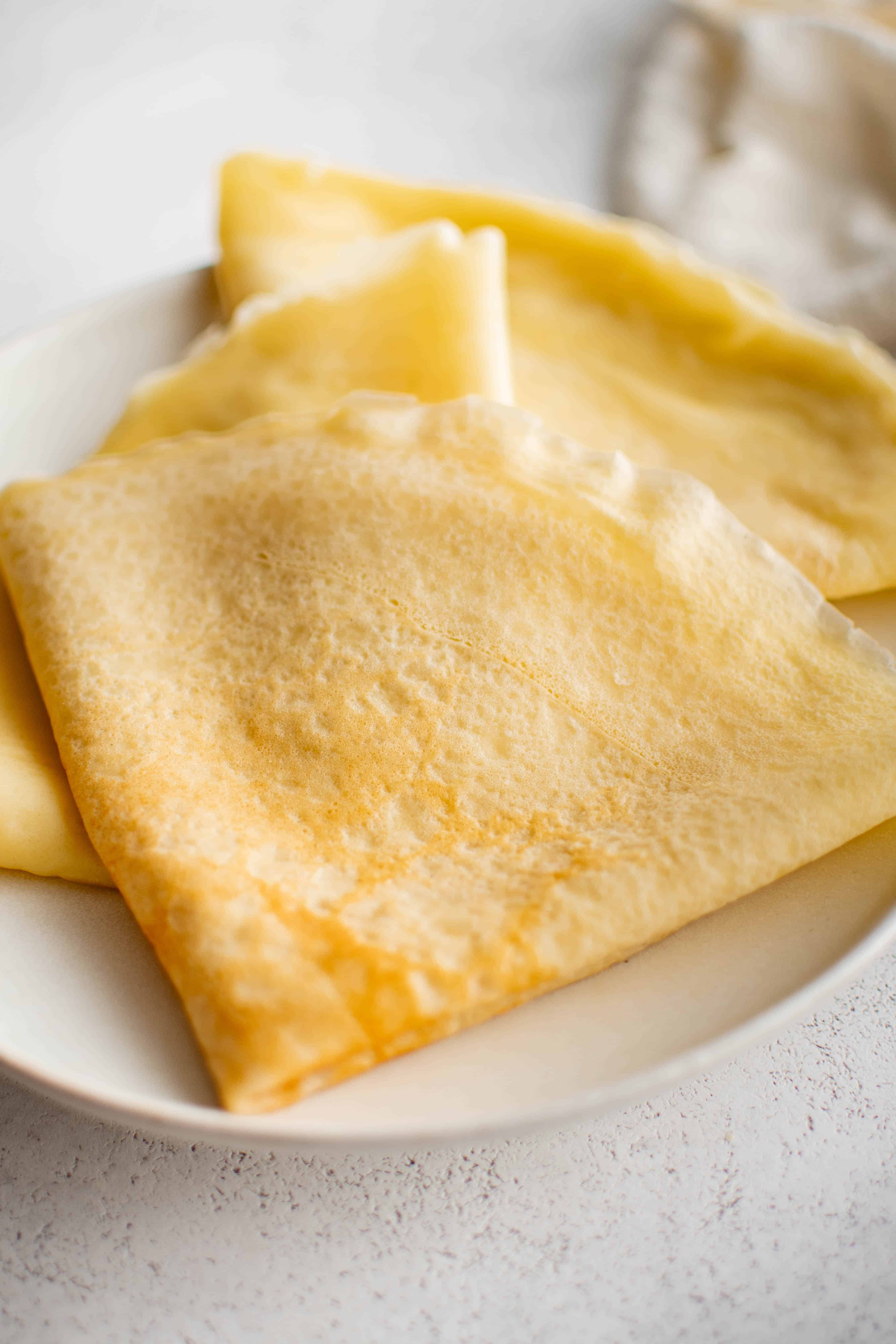Three golden crepes with crisp edges folded into quarters on a white plate.