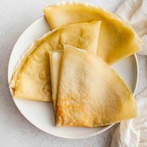 Overhead image of three golden crepes with crisp edges folded into quarters on a white plate.