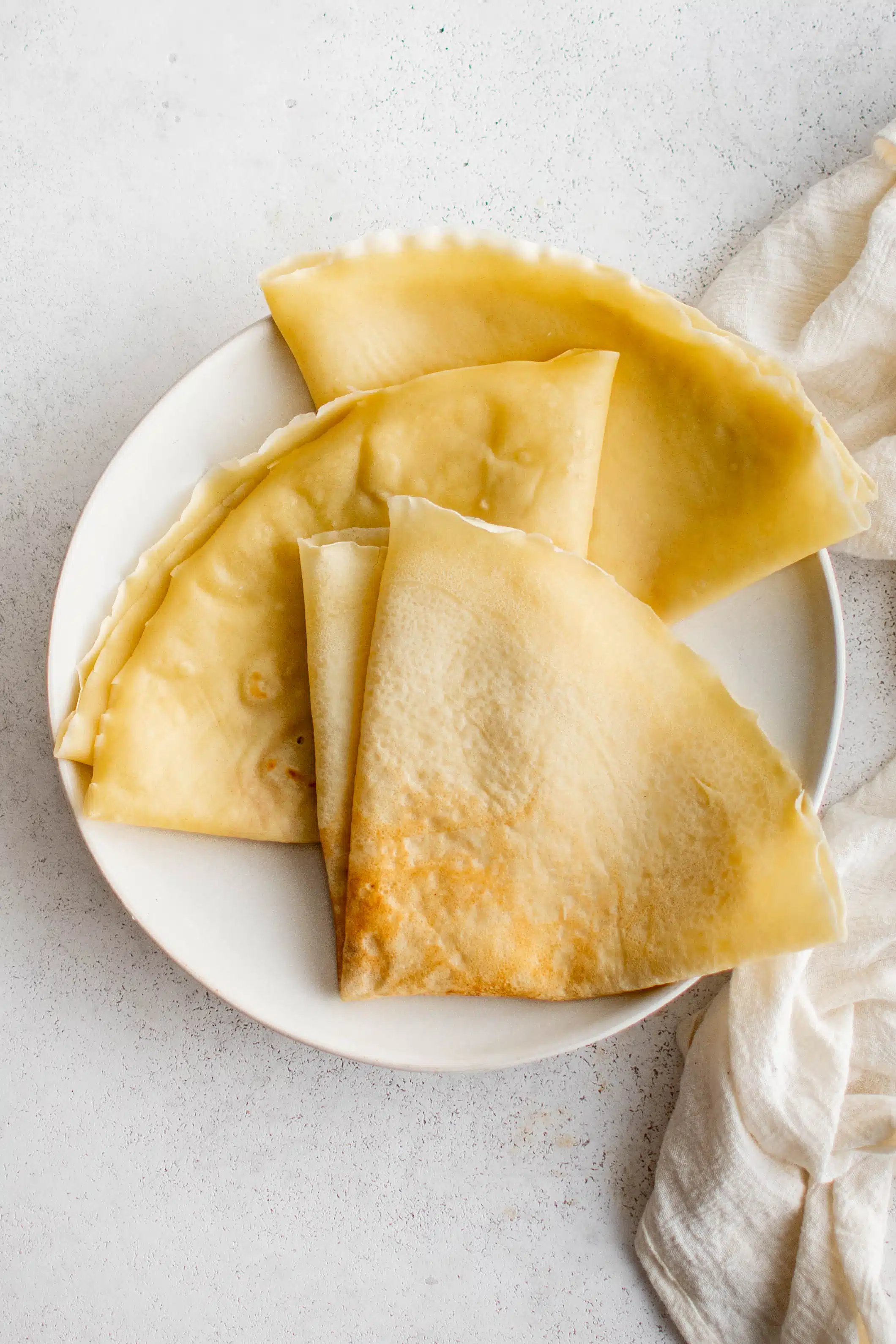 Overhead image of three golden crepes with crisp edges folded into quarters on a white plate.