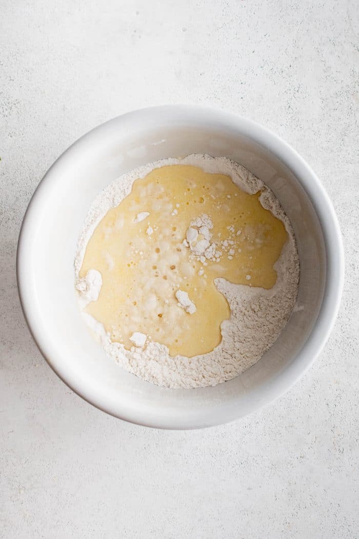 White mixing bowl filled with whisked together milk, eggs, butter, and vanilla poured on top of mixed together flour sugar and salt.