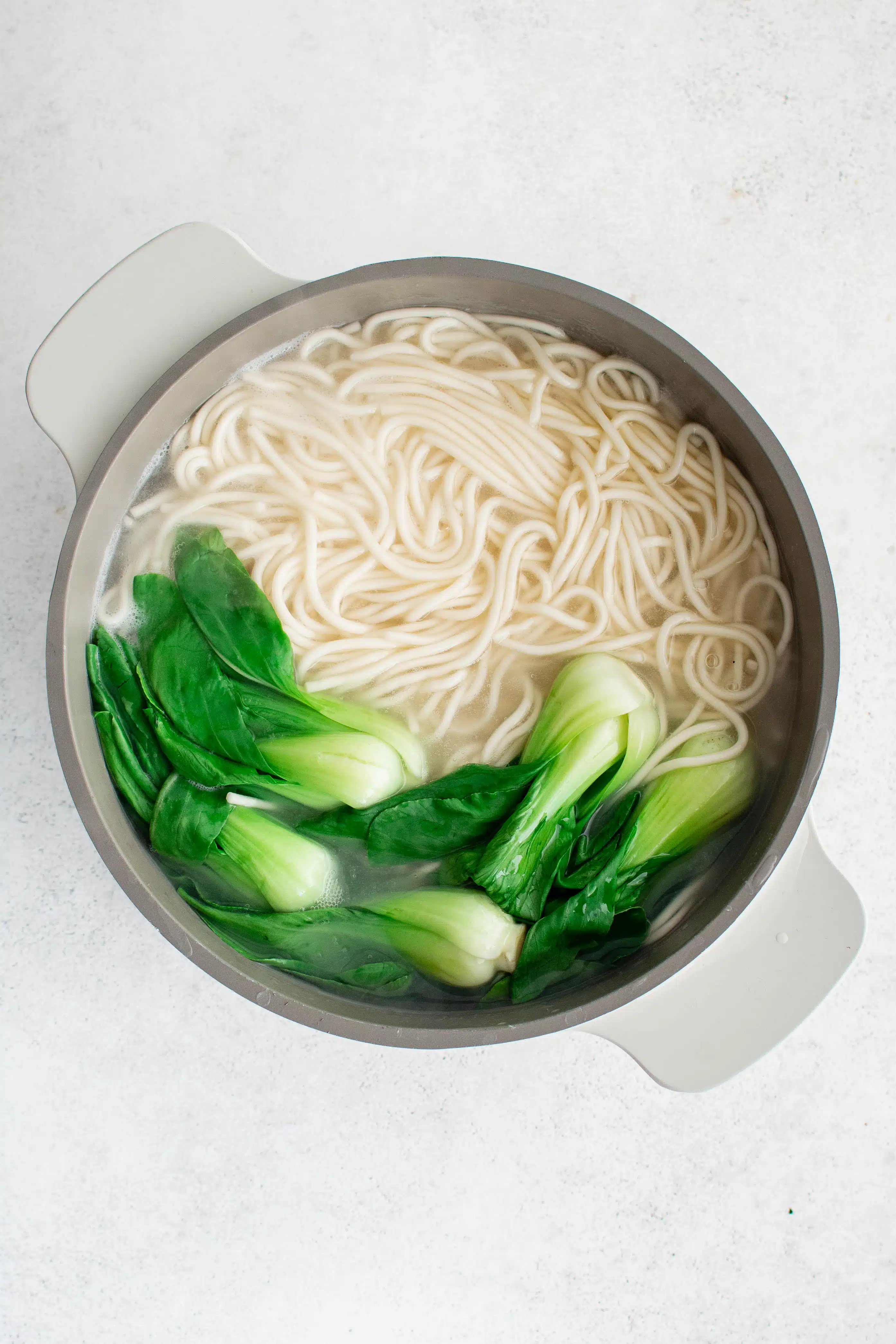 Large pot filled with boiling water with Chinese noodles and baby bok choy.