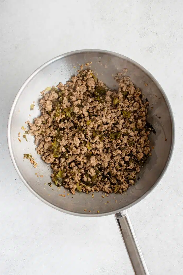 Large wok filled with cooked ground pork seasoned with garlic, wine, soy sauce, mirin, oil, ginger, and five spice.