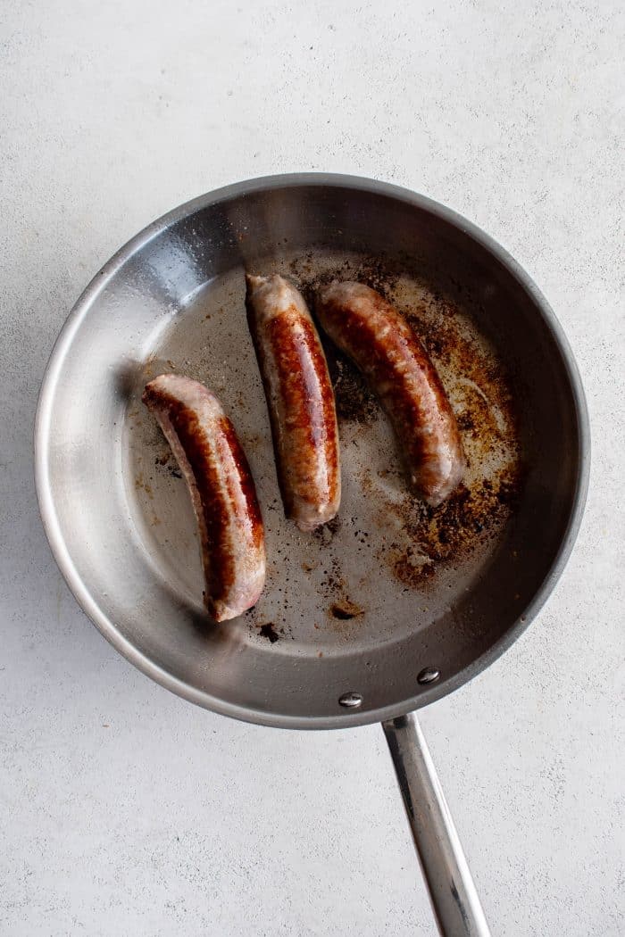 Frying pan with three charred sausages.