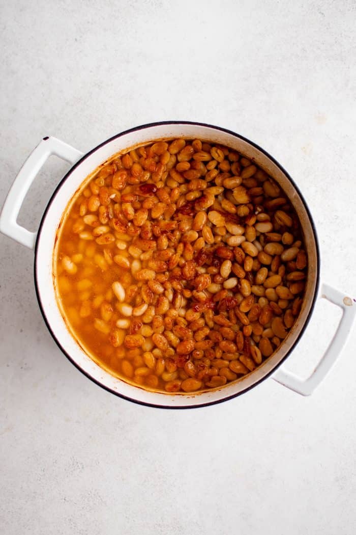 Dutch oven filled with baked beans with a golden brown crispy crust and filled with broth to cover the beans.