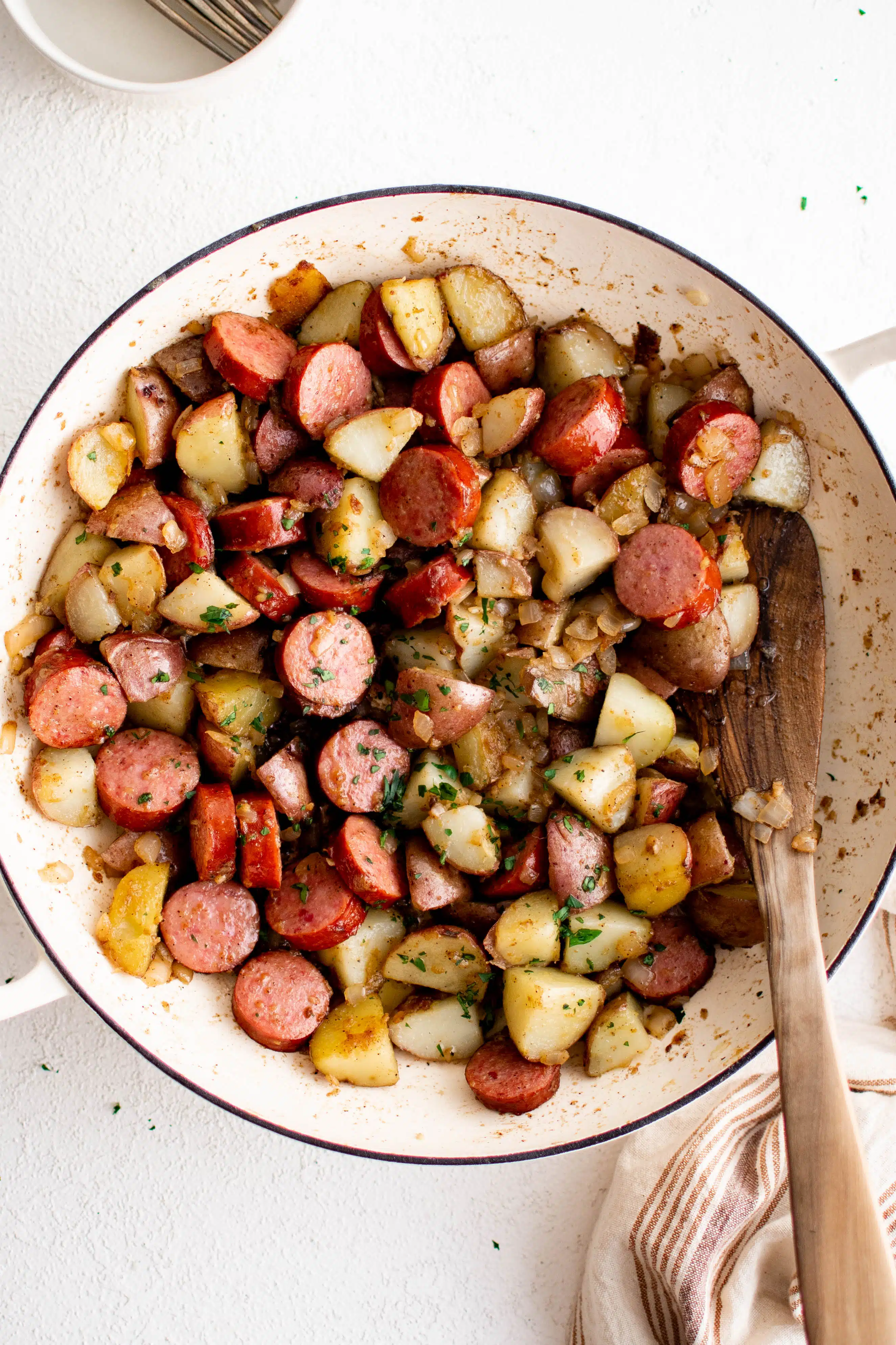 Prepared kielbasa and potatoes in a large pan garnished with chopped parsley.