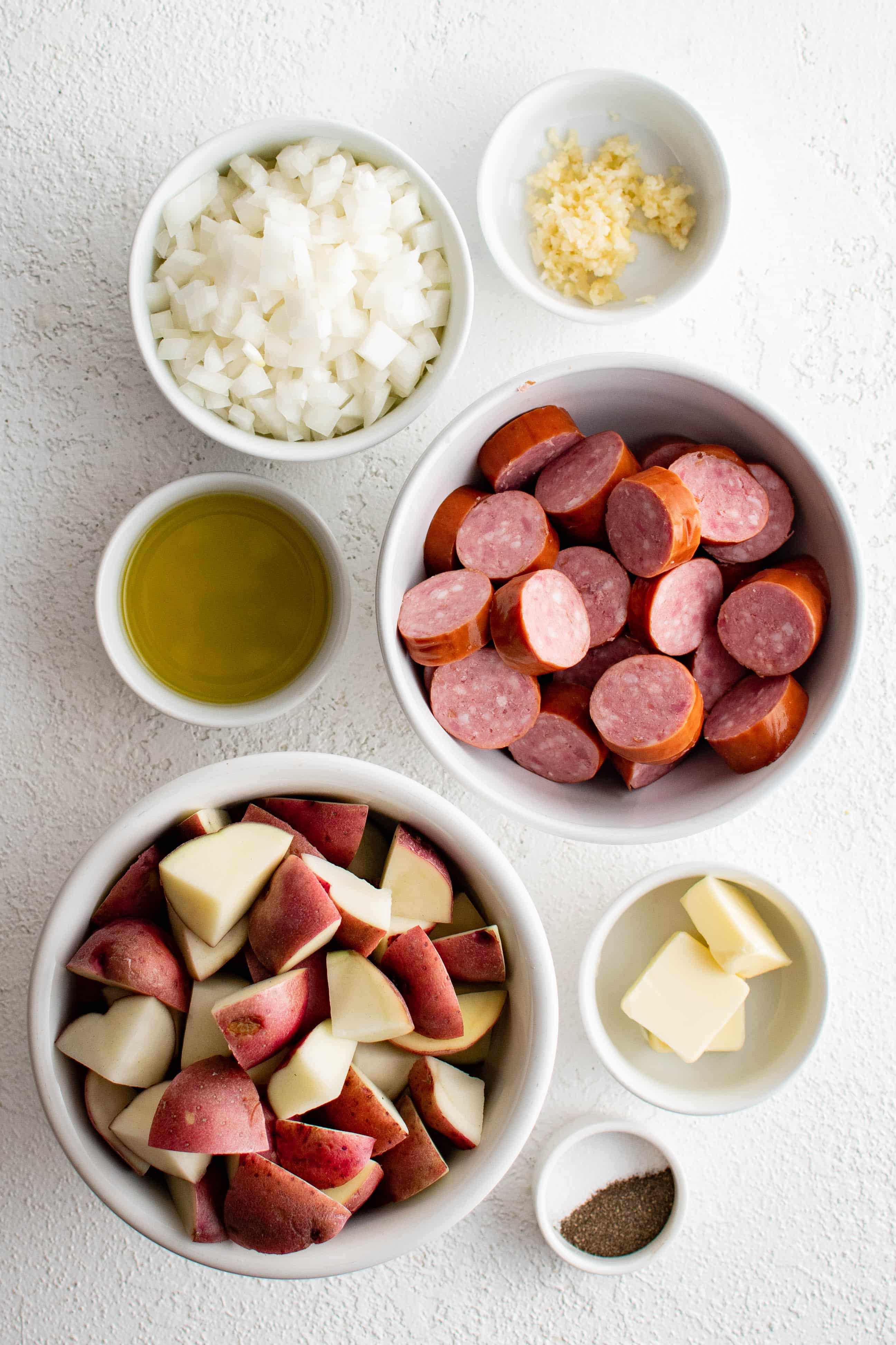 Ingredients needed to make kielbasa and potatoes in a bowl in individual measuring cups and ramekins.