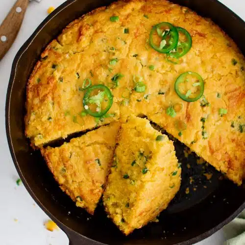 Overhead image of a cast iron skillet filled with baked sliced Mexican cornbread with diced jalapeños, Monterey Jack cheese and cheddar cheese.