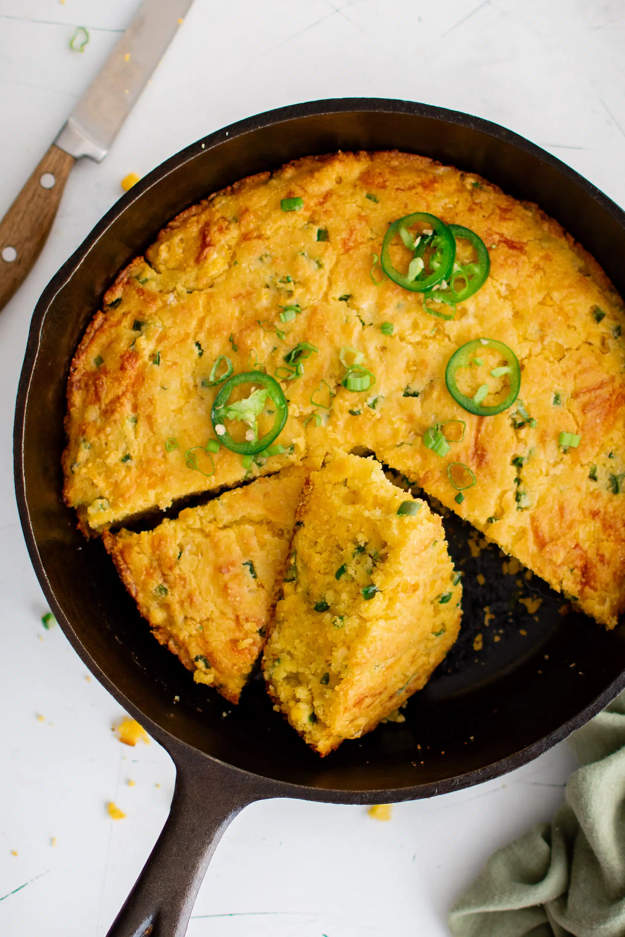 Overhead image of a cast iron skillet filled with baked sliced Mexican cornbread with diced jalapeños, Monterey Jack cheese and cheddar cheese.