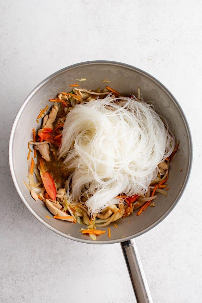Soaked glass noodles added to a large wok filled with chicken and vegetable stir fry.