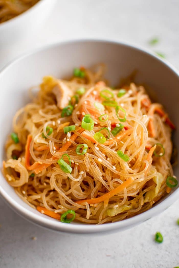 Overhead image of a white bowl filled with stir fried glass noodles with chicken and vegetables and garnished with green onions.