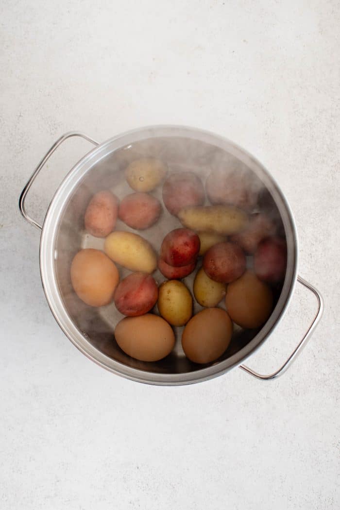 Pot filled with boiling water, baby potatoes, and four eggs.