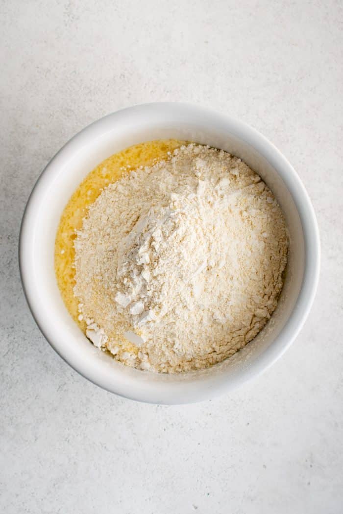 Overhead image of a white mixing bowl with the dry ingredients for sweet cornbread added to the wet ingredients.