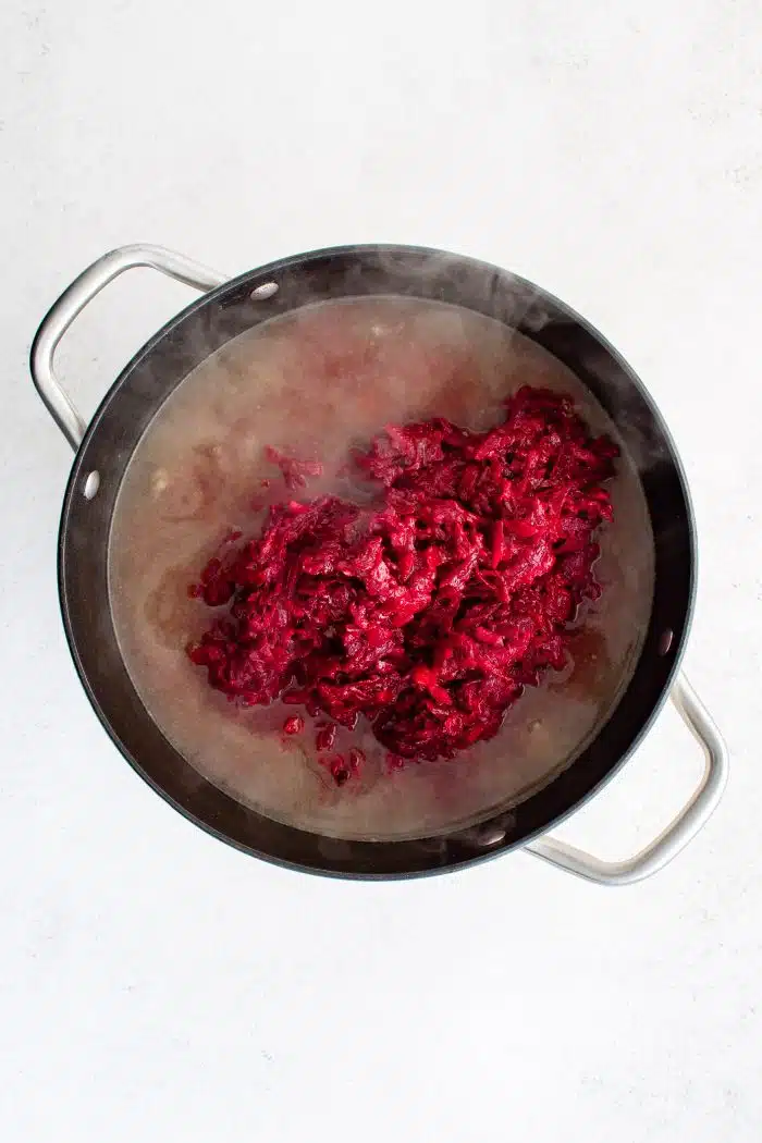 Beet mixture added to a large pot filled with tender chunks of beef and potatoes simmer in a homemade beef broth.