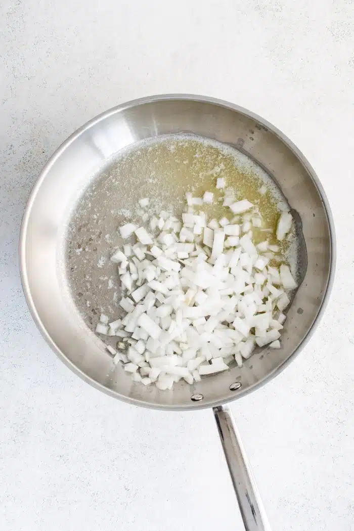 Large stainless steel skillet with olive oil and a diced white onion.