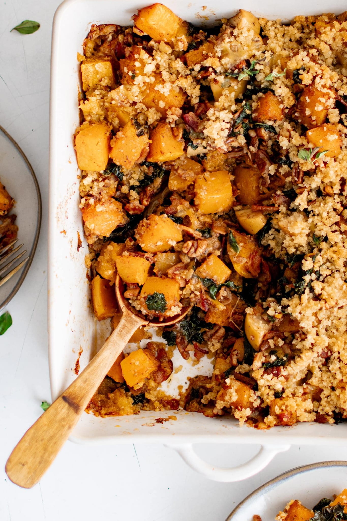 Overhead image of a large serving spoon digging into a large white casserole dish filled with butternut squash casserole.
