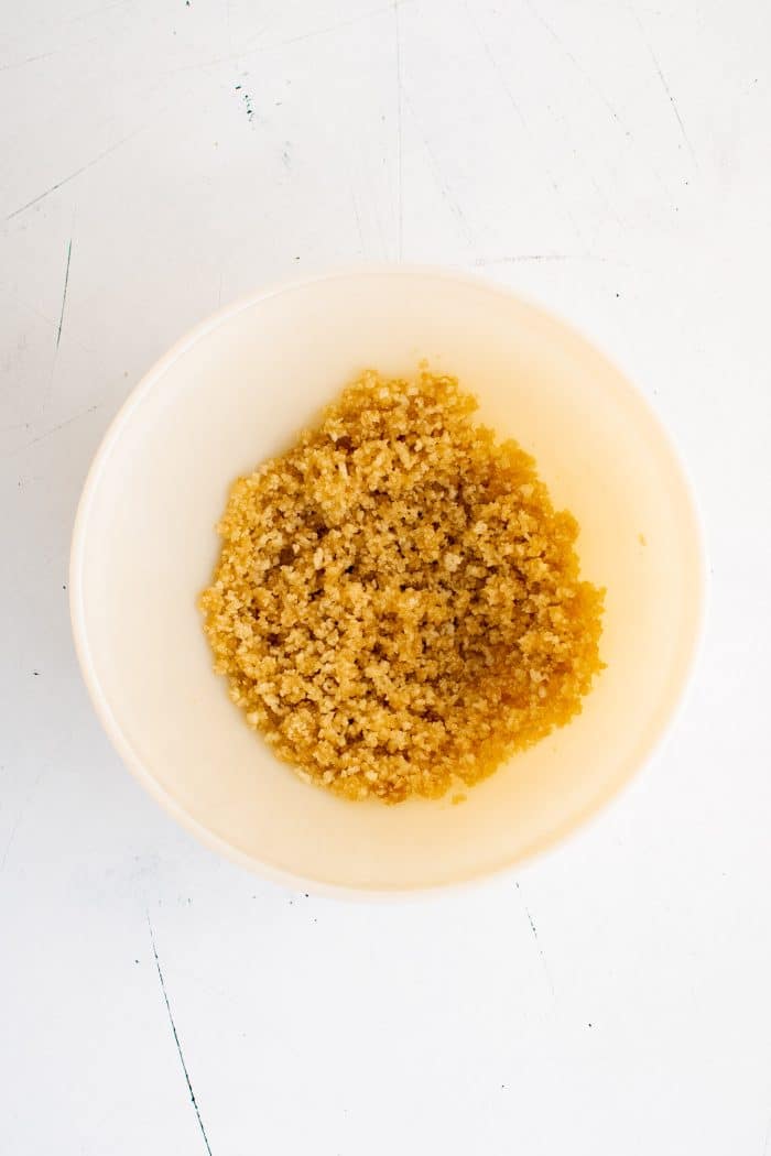 White mixing bowl filled with panko breadcrumbs combined with melted butter and maple syrup.