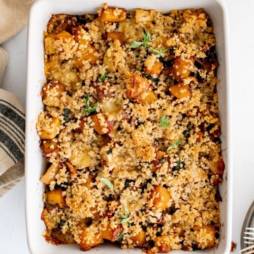 Large white baking dish filled with homemade butternut squash casserole filled with bacon, pecans, kale, apples, and cheese, and topped with maple butter panko breadcrumbs.