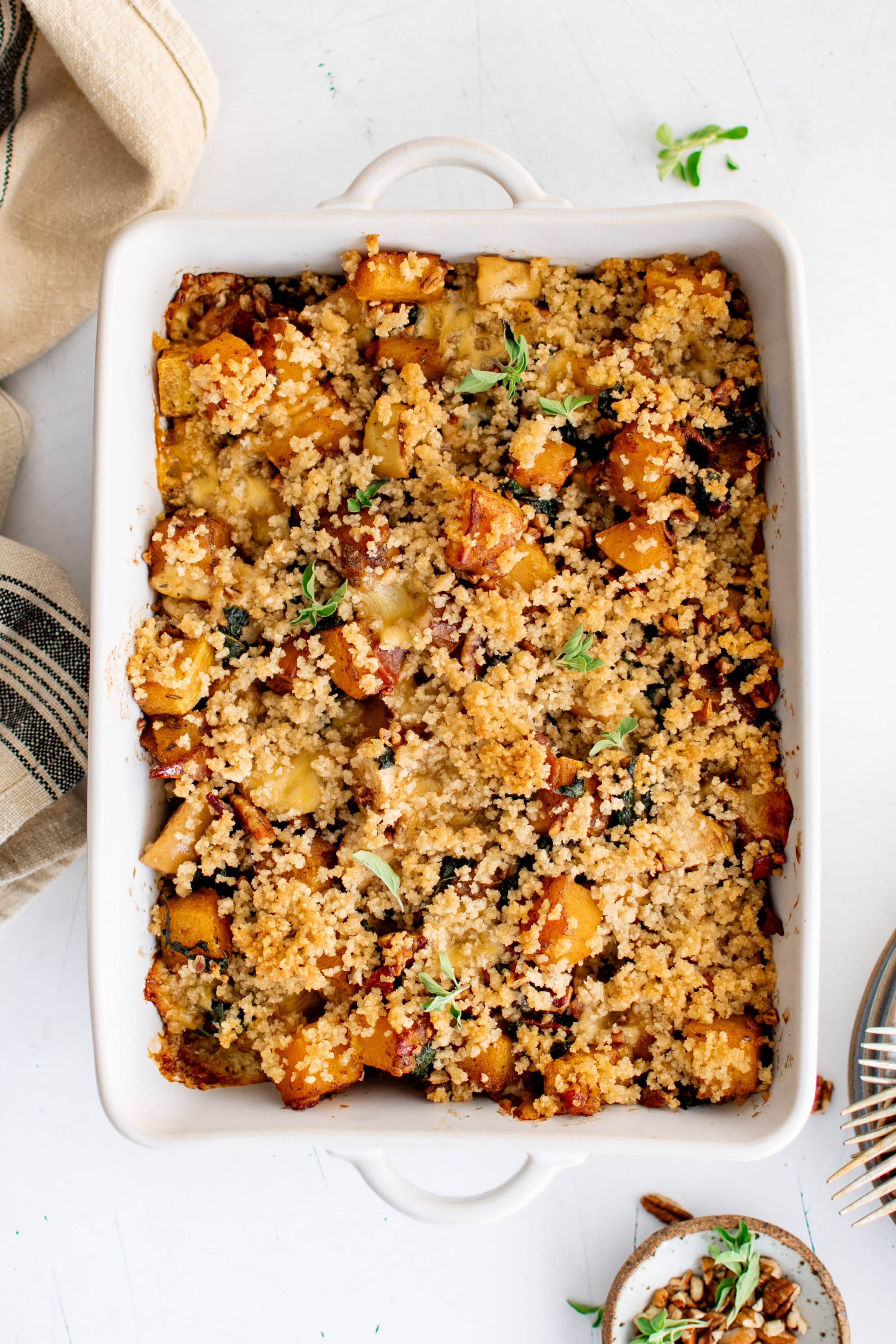 Large white baking dish filled with homemade butternut squash casserole filled with bacon, pecans, kale, apples, and cheese, and topped with maple butter panko breadcrumbs.