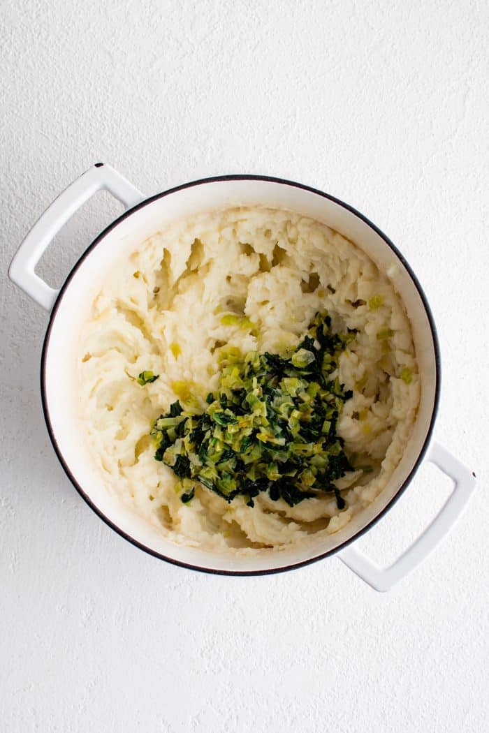 Sautéed kale and leeks added to a large pot of creamy mashed potatoes.