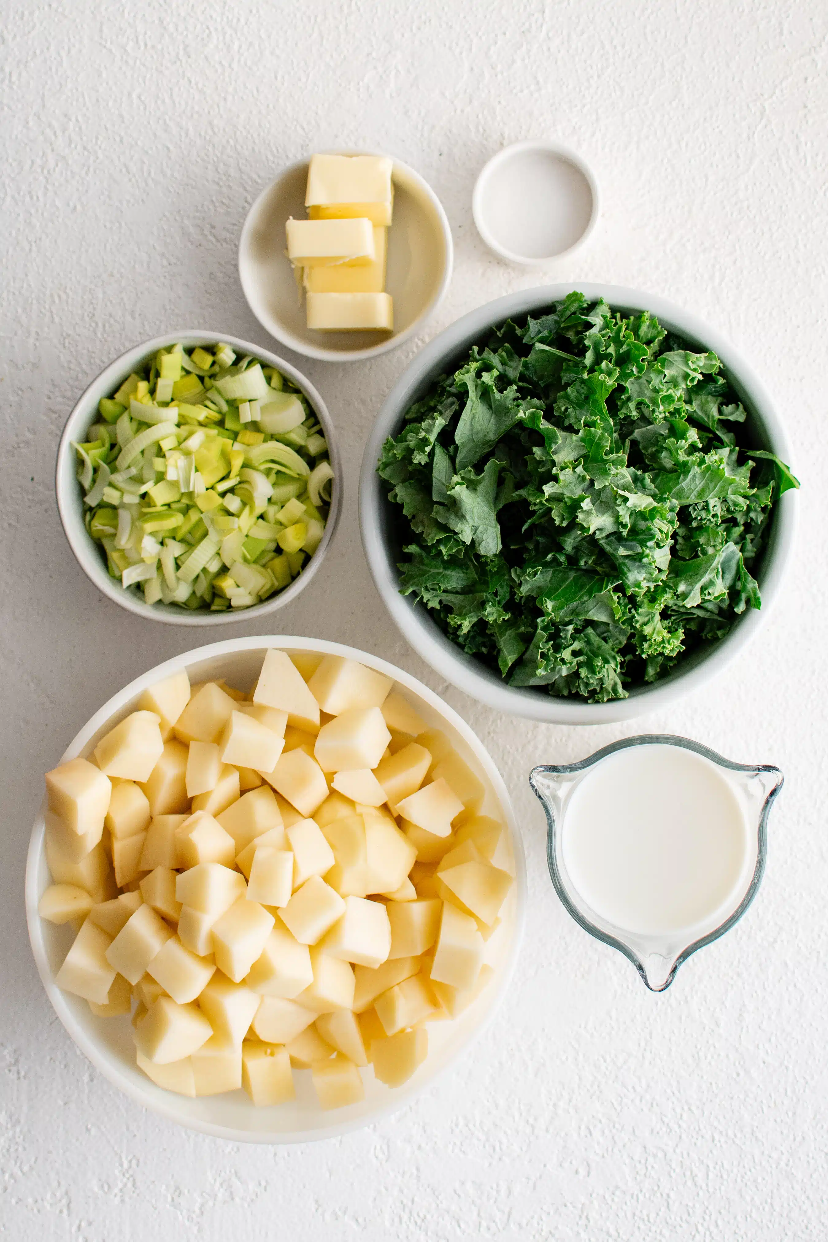 Ingredients needed to make Colcannon recipe in a bowl in individual measuring cups and ramekins.