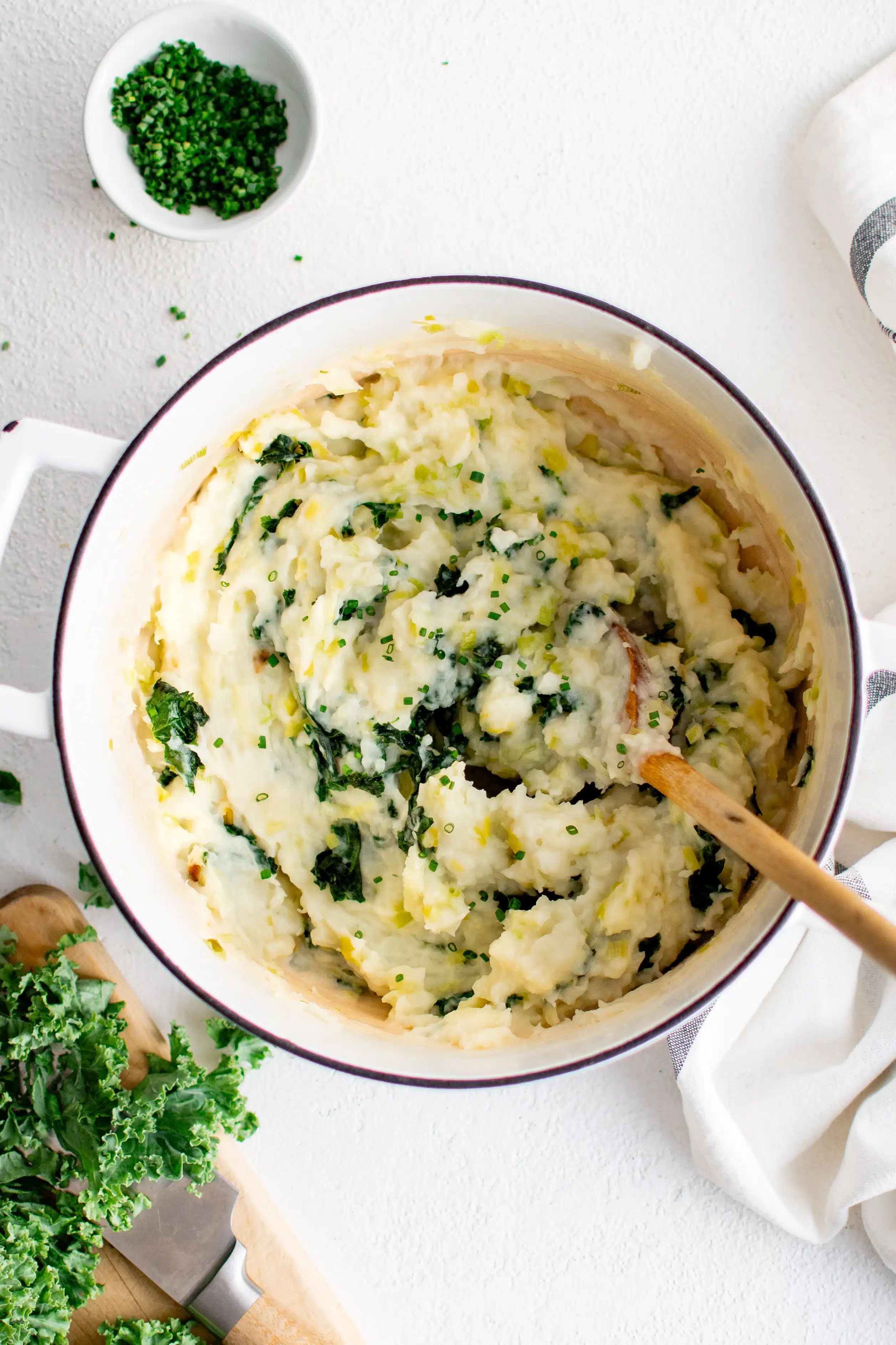 Large white pot filled with creamy mashed colcannon made with mashed potatoes and sauteed kale and leeks.