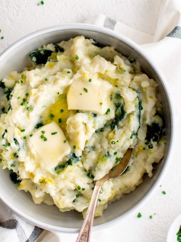 Large white serving bowl filled with colcannon with kale and leeks and topped with to melting pats of butter.