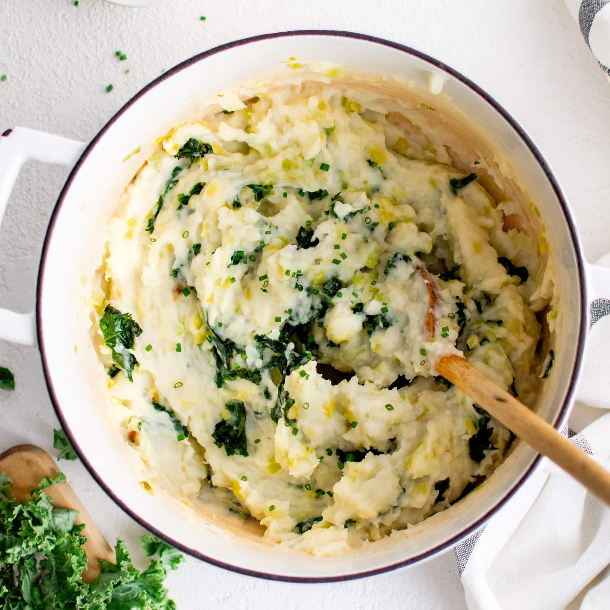 Large white pot filled with creamy mashed colcannon made with mashed potatoes and sautéed kale and leeks.