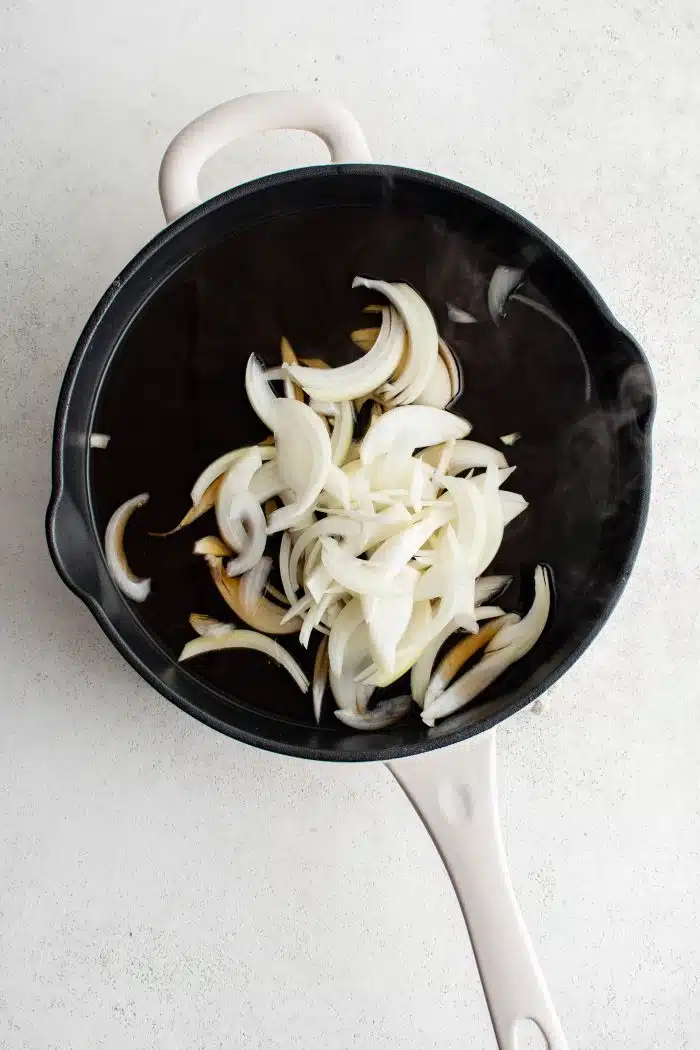 Large pan filled with thinly sliced raw white onion.