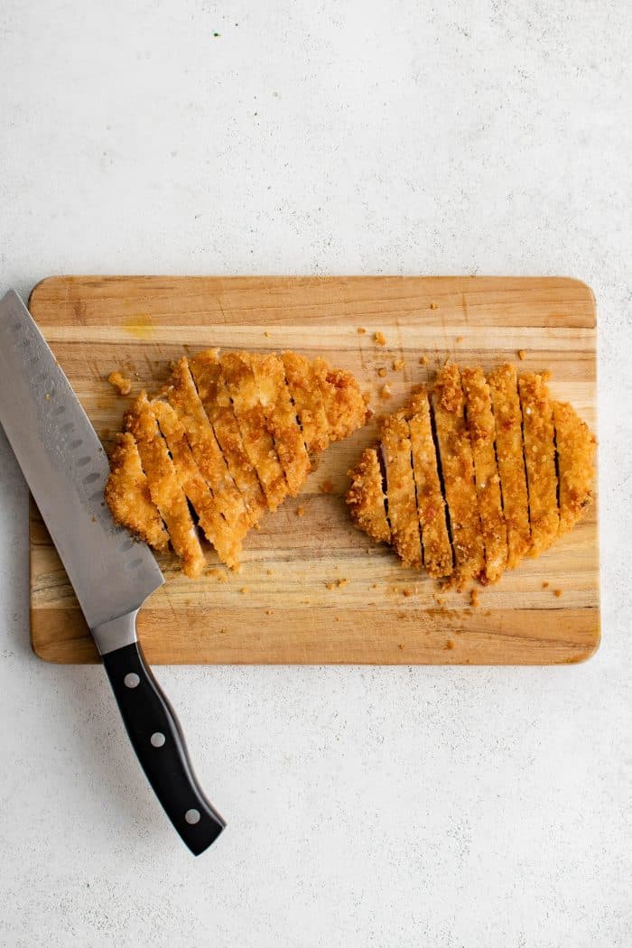 Overhead image of a large cutting board showing two perfectly sliced crispy katsu (breaded and deep fried pork cutlets).