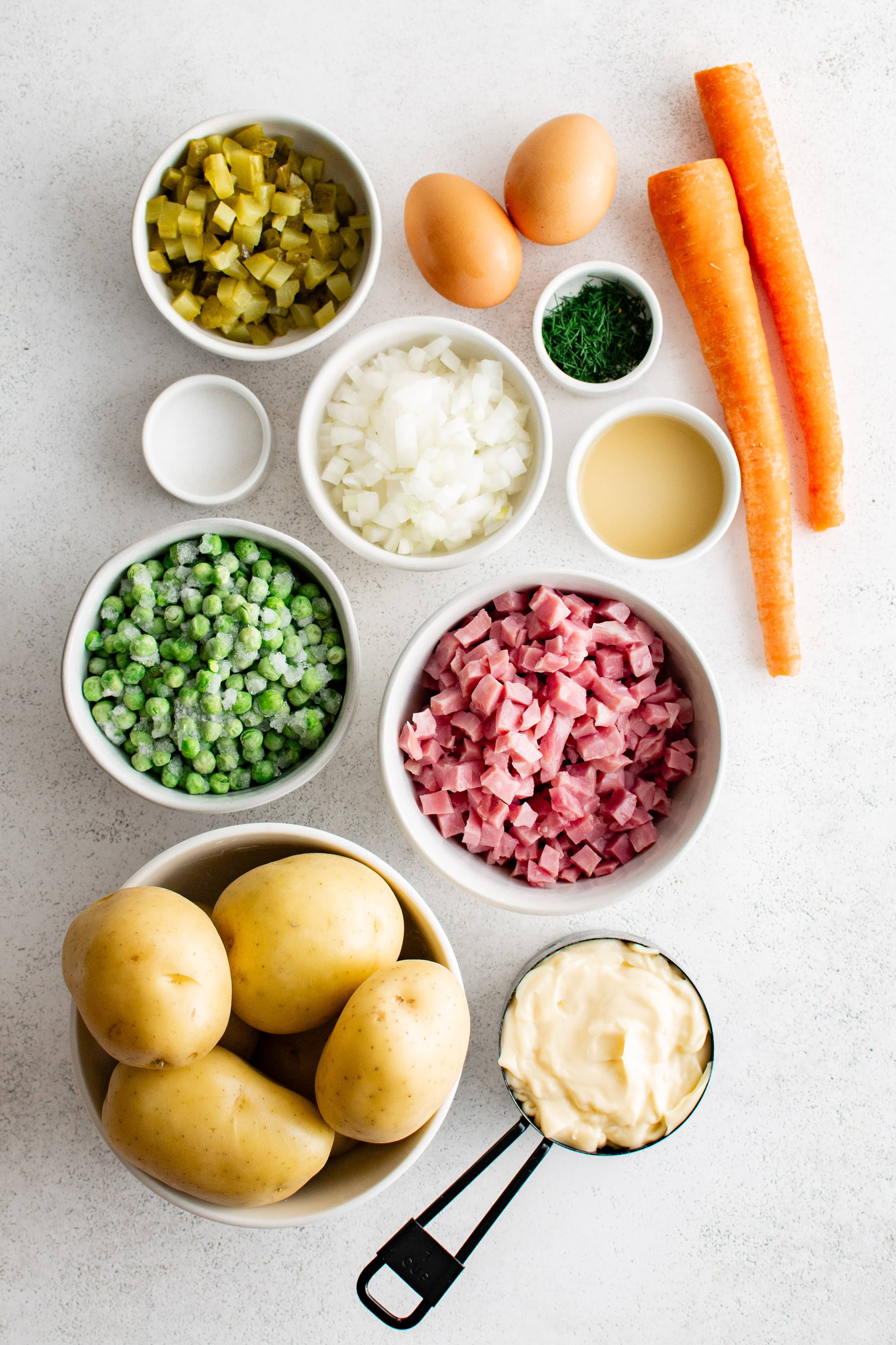 Ingredients needed to make homemade Olivier salad in individual measuring cups and ramekins.