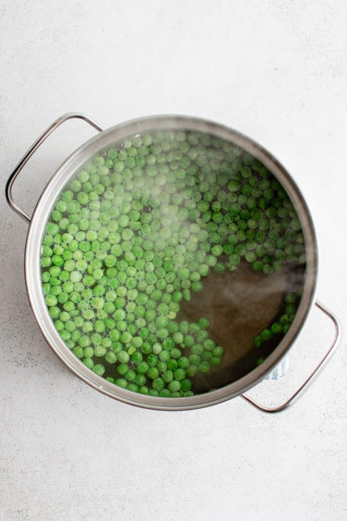 Frozen green peas reheating in a large pot filled with boiling water.