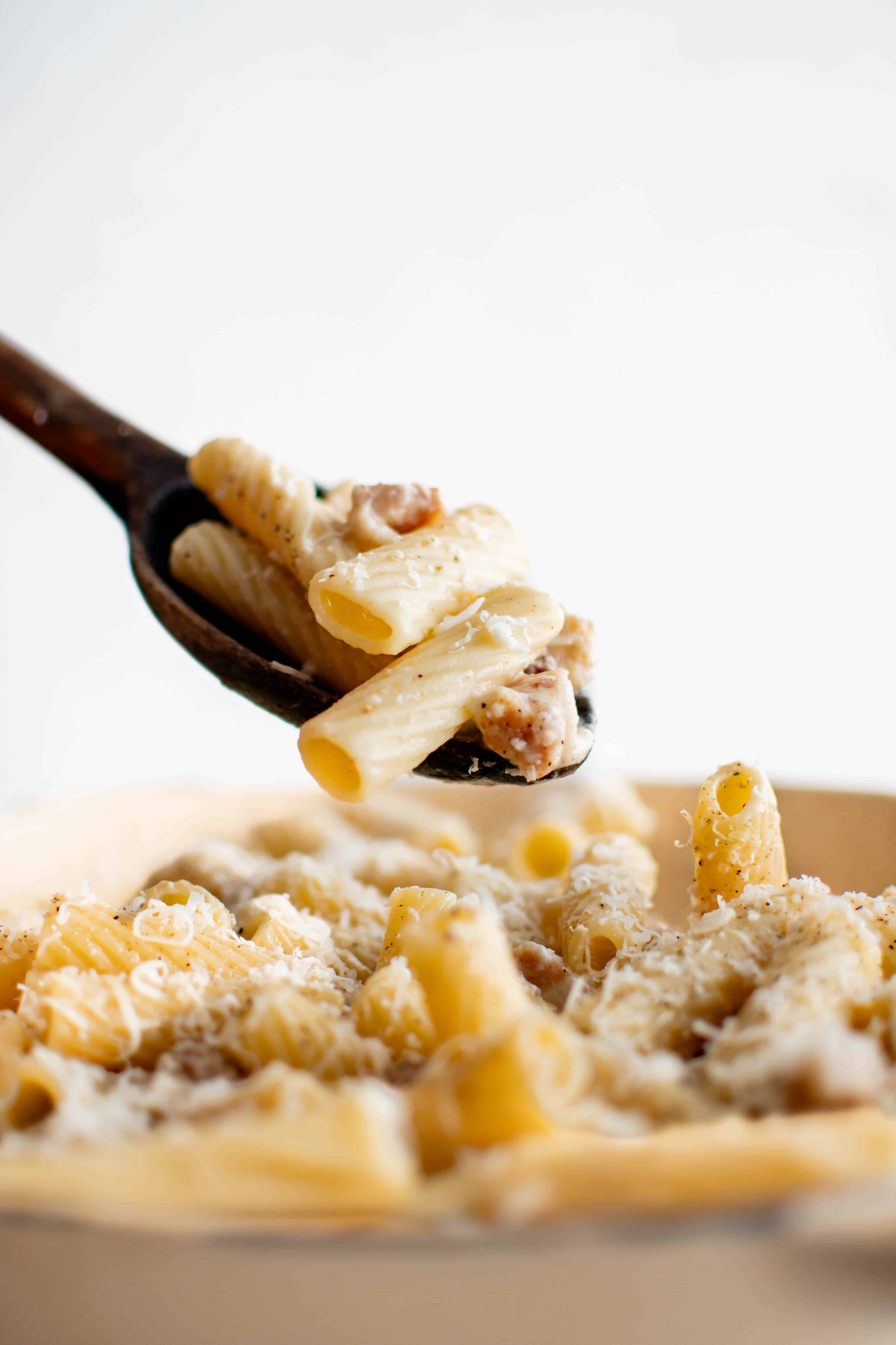 Large spoon filled with a serving of rigatoni alla gricia hovering over a pan filled with fully cooked and prepared pasta.