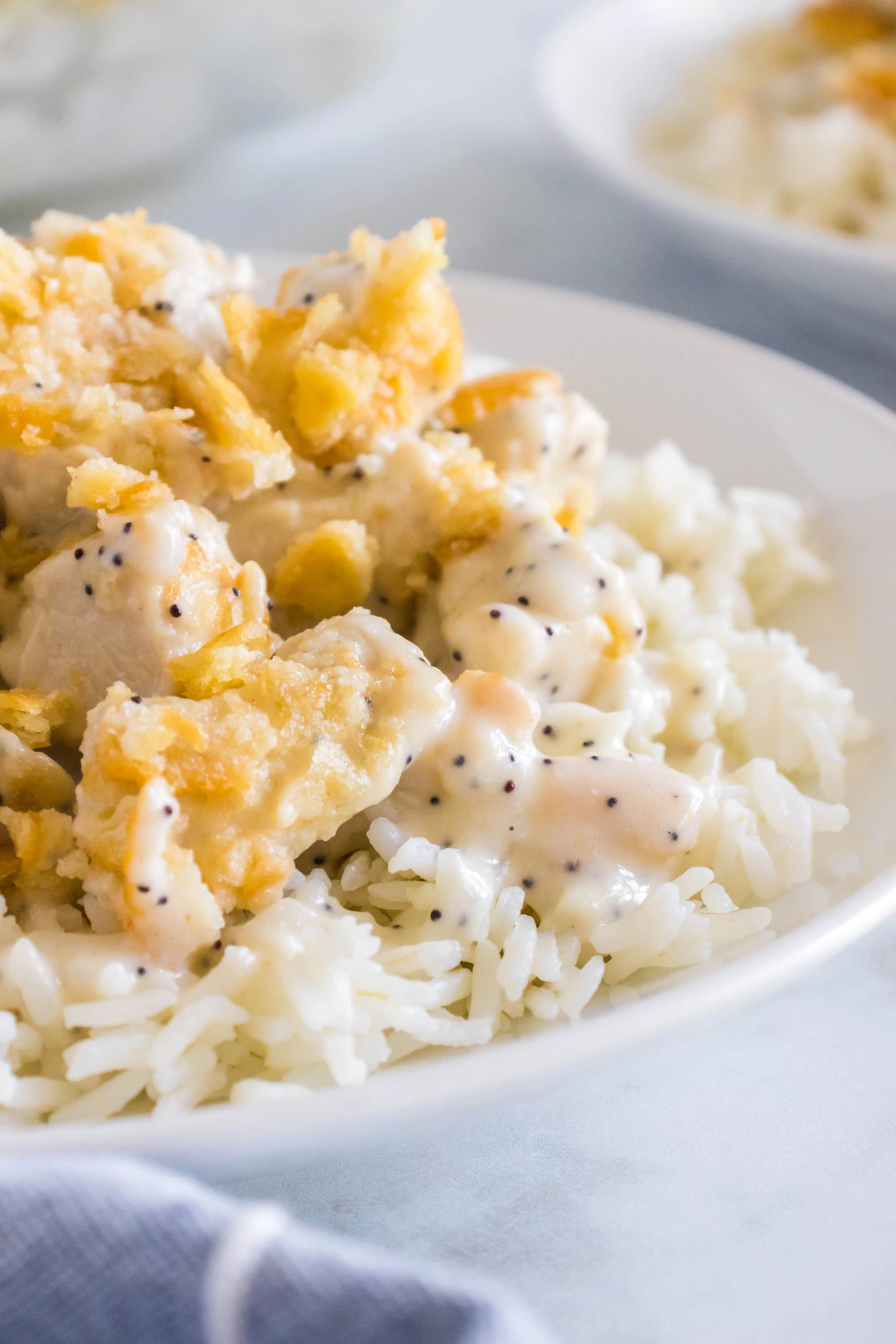 Cooked white rice on a white dinner plate and topped with creamy, saucy poppy seed chicken casserole.