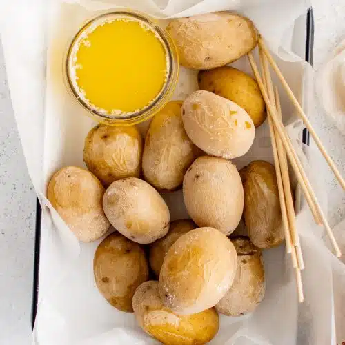 Tender cooked baby potatoes with a salt crust and soft insides arranged in a small baking dish line with parchment paper and served with a small side of melted butter.