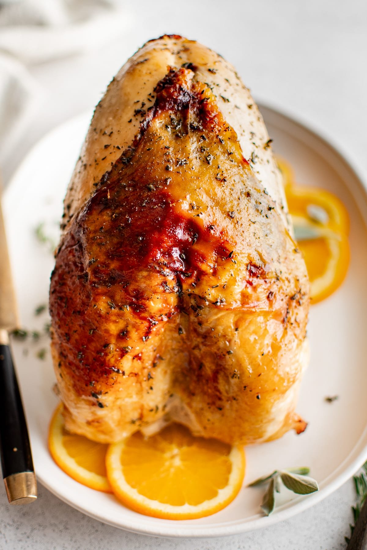Whole roasted turkey breast with golden brown skin served on a platter with orange slices.