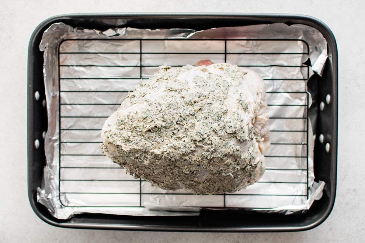 Raw turkey breast coated in herb butter placed on a rack in a roasting pan.
