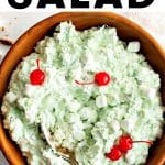 Large wooden bowl filled with the pistachio-flavored salad, garnished with mini marshmallows and maraschino cherries, and a large spoon ready to serve. The text overlay reads โWatergate Saladโ